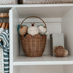 Two children wearing sandals and dresses stood on the grass holding Olli Ella Rattan Tulip Carry Basket - Seashell Pink and Natural filled with flowers from the garden
