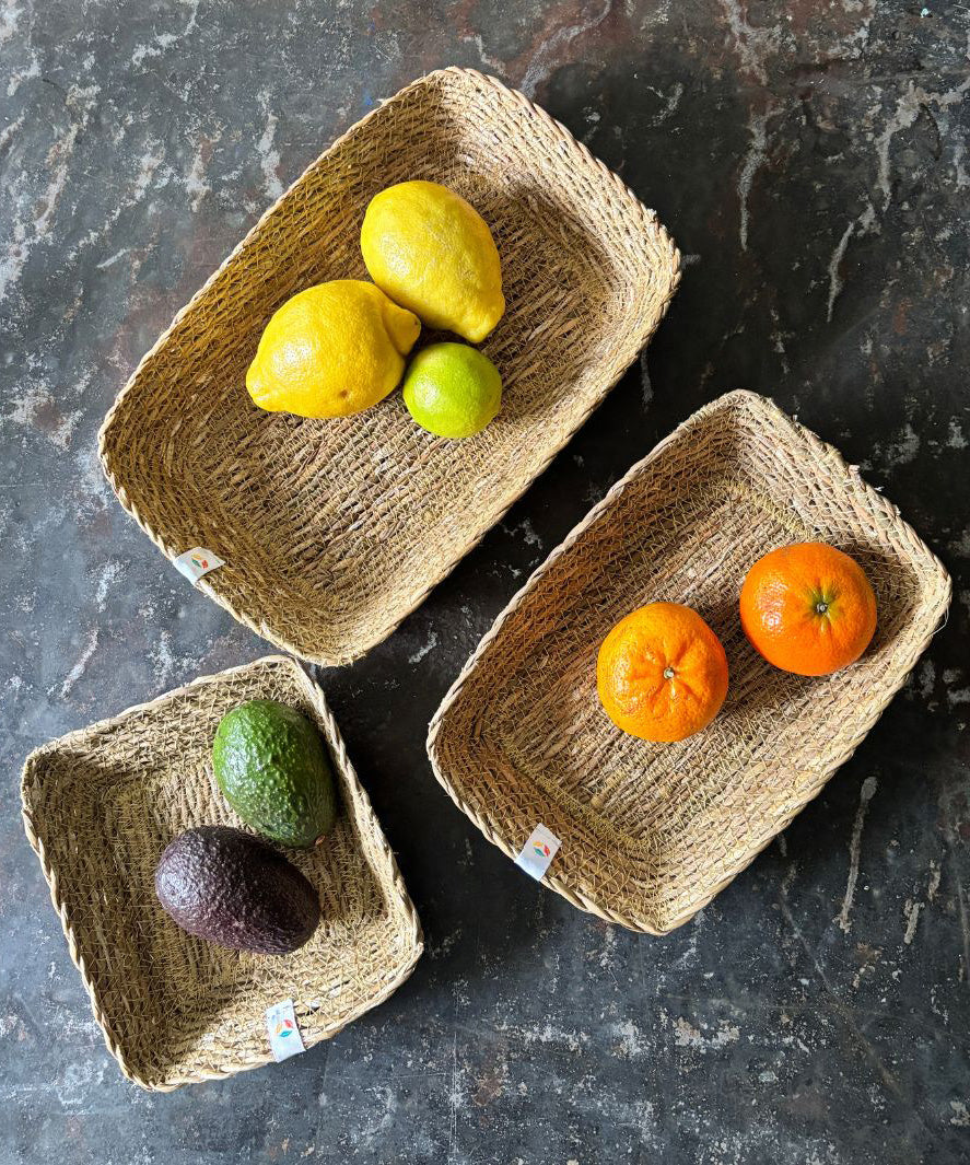 A top down view of the Respiin rectangular seagrass baskets on top of a stone surface with fruit inside each basket