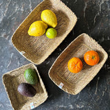 A top down view of the Respiin rectangular seagrass baskets on top of a stone surface with fruit inside each basket