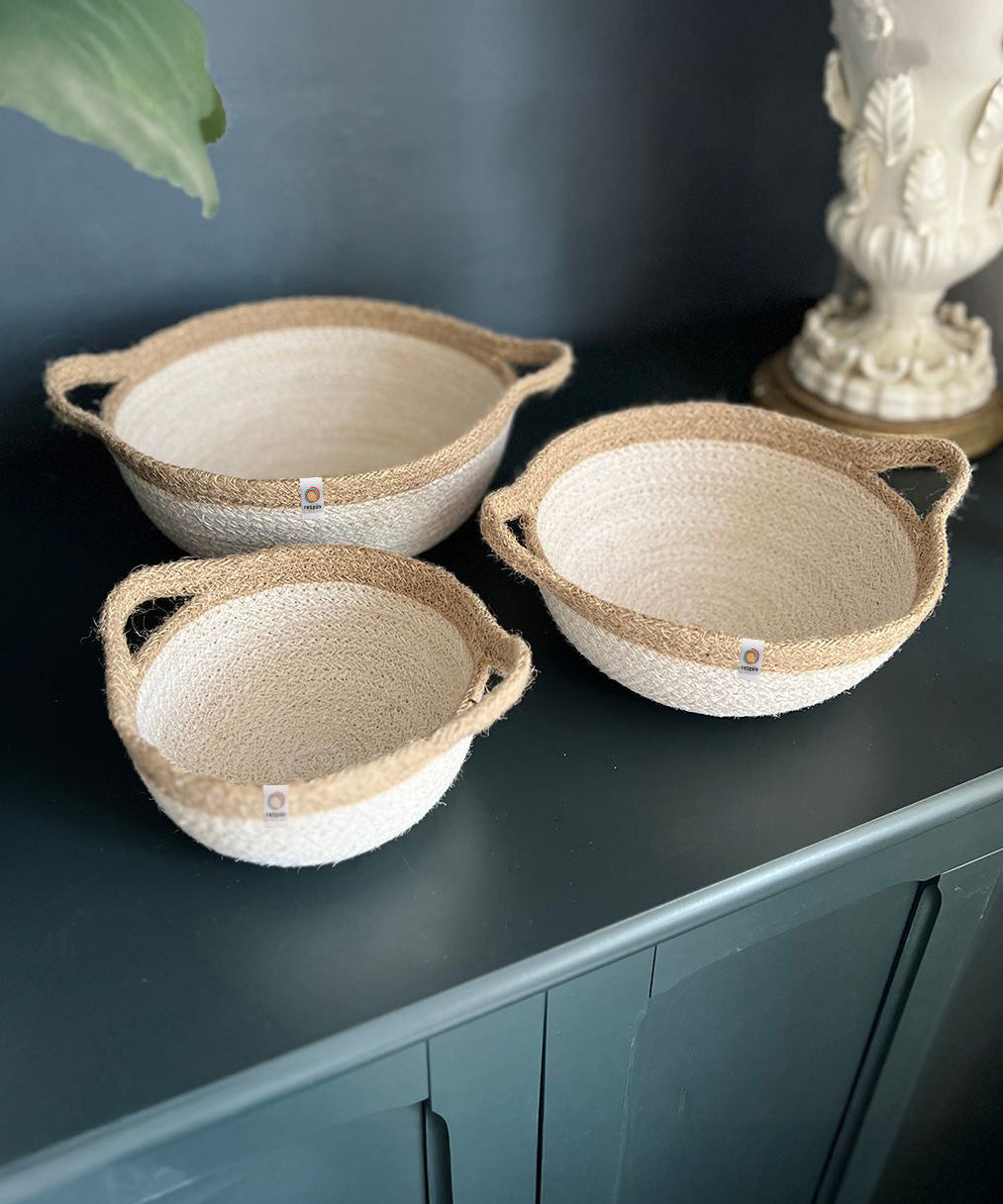 A set of 3 Respiin jute handled bowls in white and natural on top of a wooden dresser.