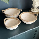 A set of 3 Respiin jute handled bowls in white and natural on top of a wooden dresser.
