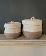 Respiin natural jute lidded basket set in white and natural colourway standing next to each other upright on a stone shelf