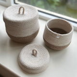 Respiin natural jute lidded basket set. A set of 2 white and natural baskets on a windowsill with the lid off the smallest basket