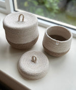Respiin natural jute lidded basket set. A set of 2 white and natural baskets on a windowsill with the lid off the smallest basket