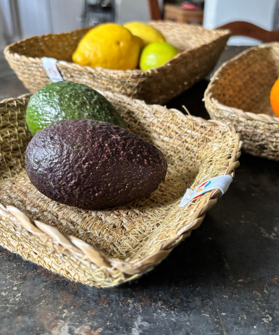A close up view of the Respiin rectangular seagrass baskets inside eachother on top of a stone surface showing the woven detail and fruit in each basket