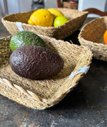 A close up view of the Respiin rectangular seagrass baskets inside eachother on top of a stone surface showing the woven detail and fruit in each basket