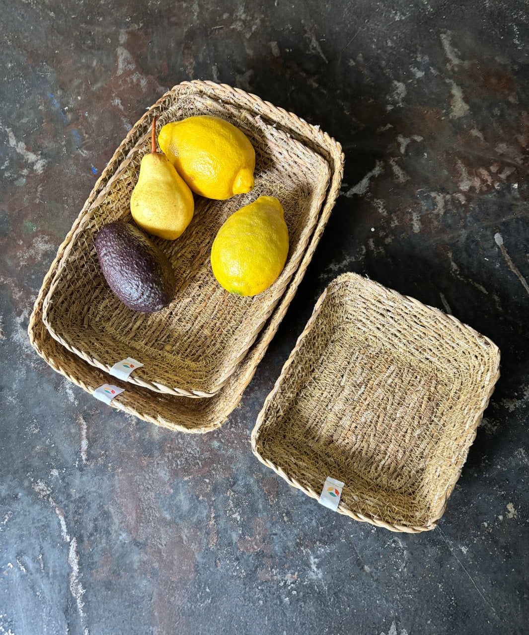 A top down view of the Respiin rectangular seagrass baskets on top of a stone surface with fruit inside the middle sized basket