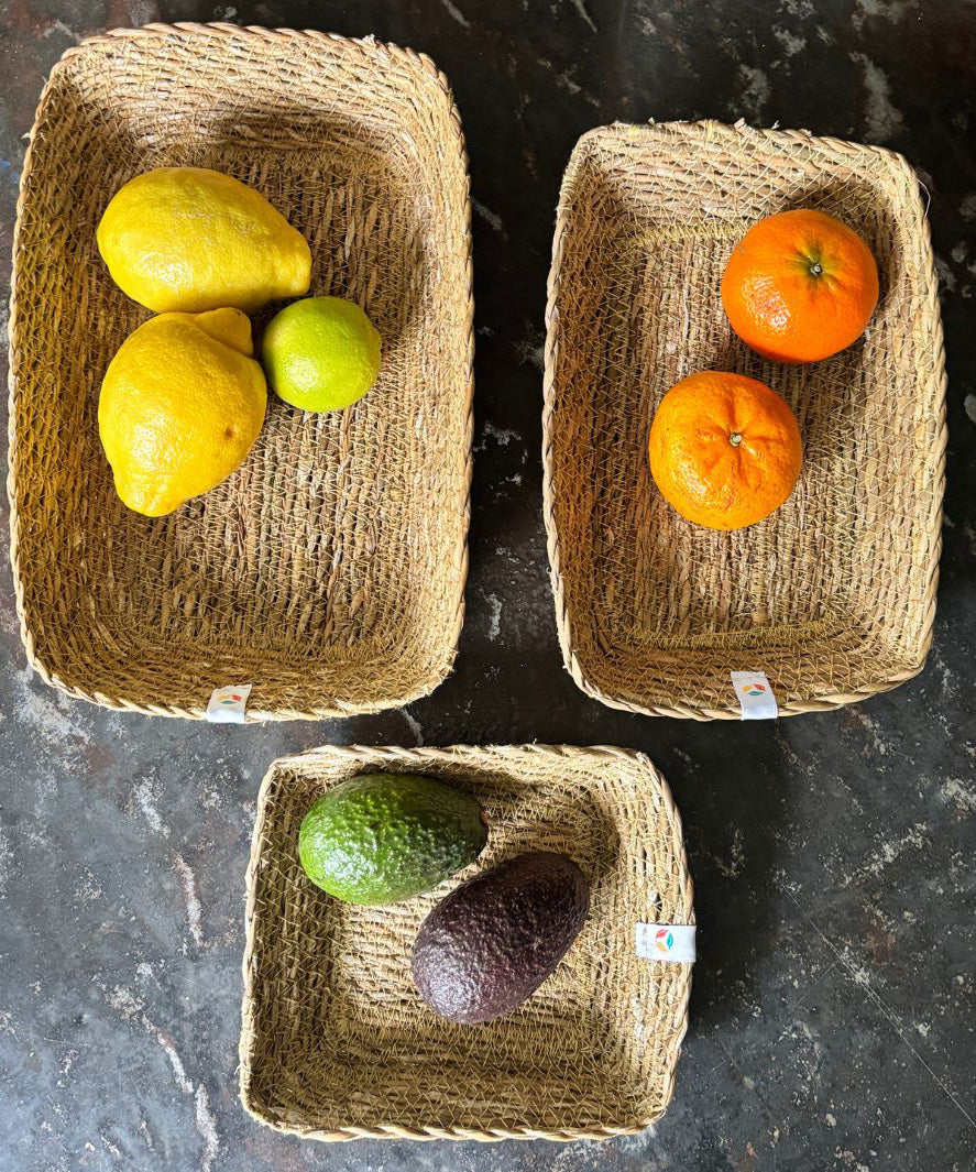 A top down view of the Respiin seagrass rectangular baskets on top of a stone surface with fruit inside each basket