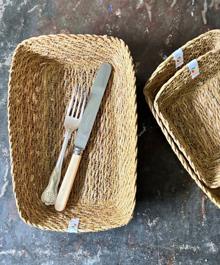 A top down view of the Respiin rectangular seagrass baskets on top of a stone surface with cutlery inside the bigger basket