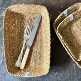 A top down view of the Respiin rectangular seagrass baskets on top of a stone surface with cutlery inside the bigger basket