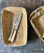 A top down view of the Respiin rectangular seagrass baskets on top of a stone surface with cutlery inside the bigger basket