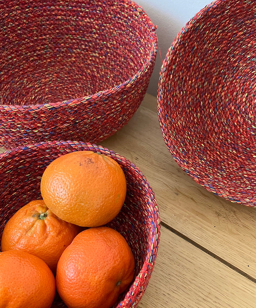 A close up of the 3 Respiin multicoloured recycled cotton bowls on a wooden surface showing the weave detail and holding fruit