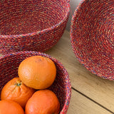 A close up of the 3 Respiin multicoloured recycled cotton bowls on a wooden surface showing the weave detail and holding fruit