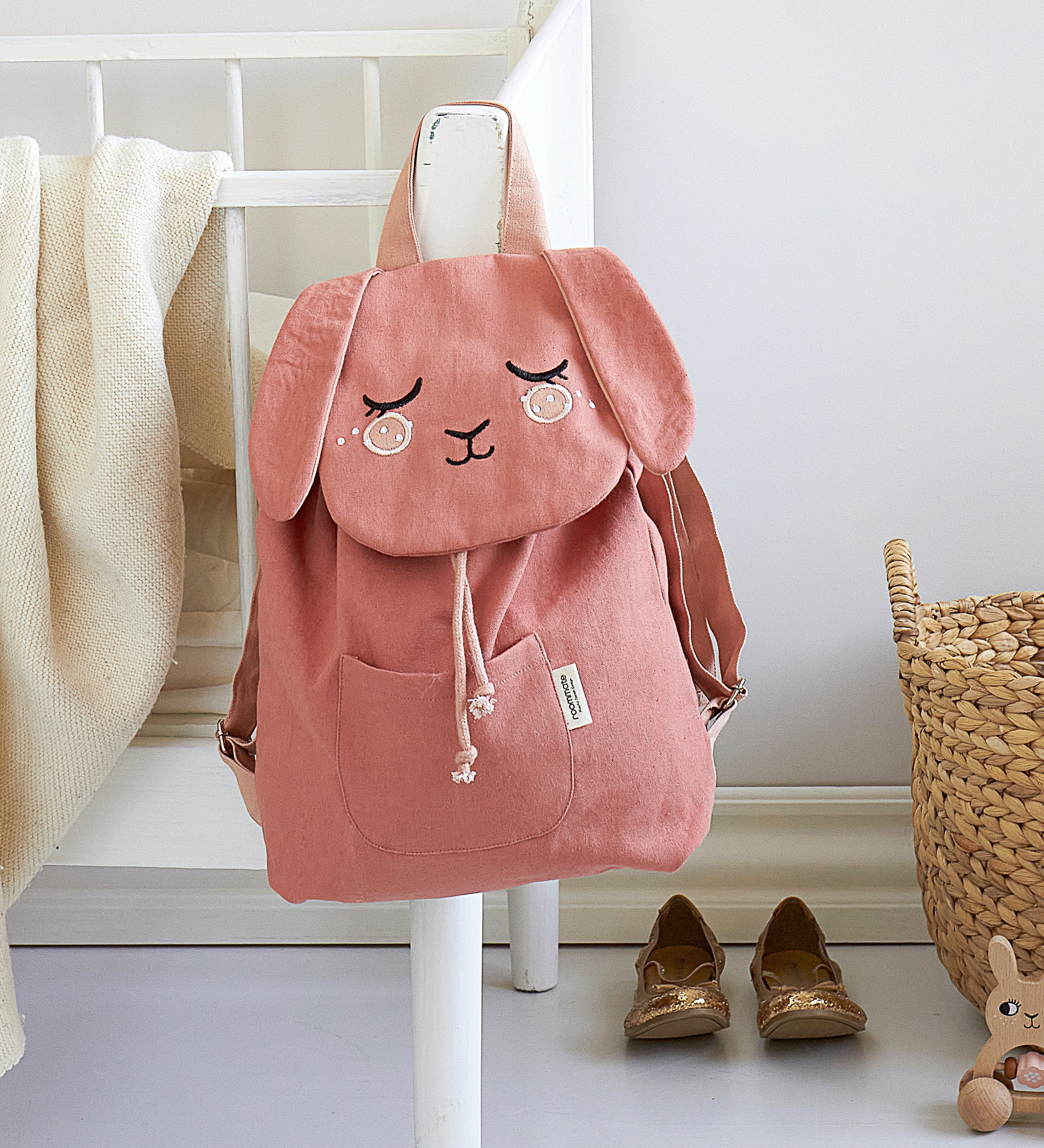 The Roommate Pink Bunny canvas backpack, hanging on a bed frame.