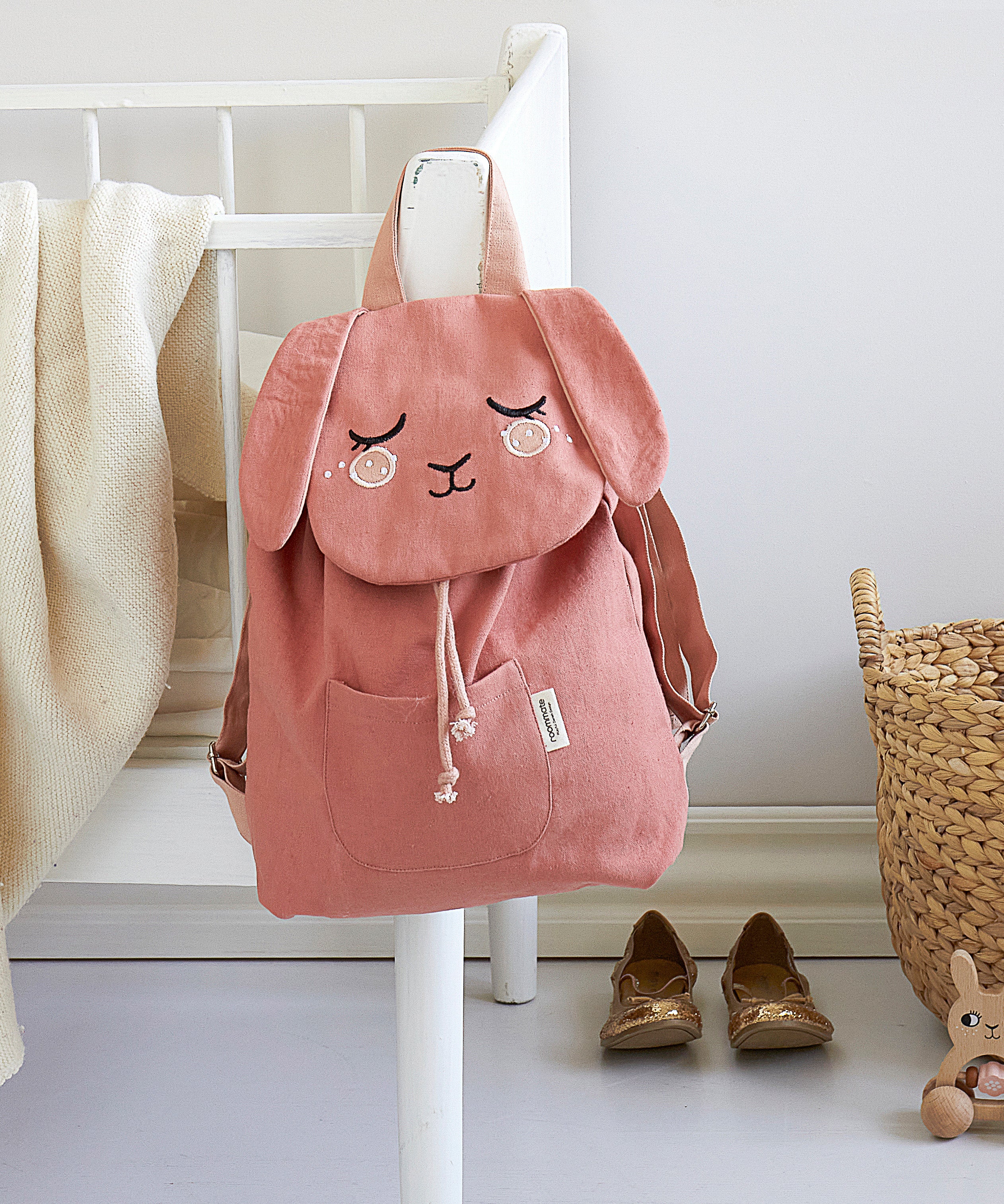 The Roommate Pink Bunny canvas backpack, hanging on a bed frame.