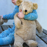 A young child holding the large Senger beige bear in the crook of their arm.