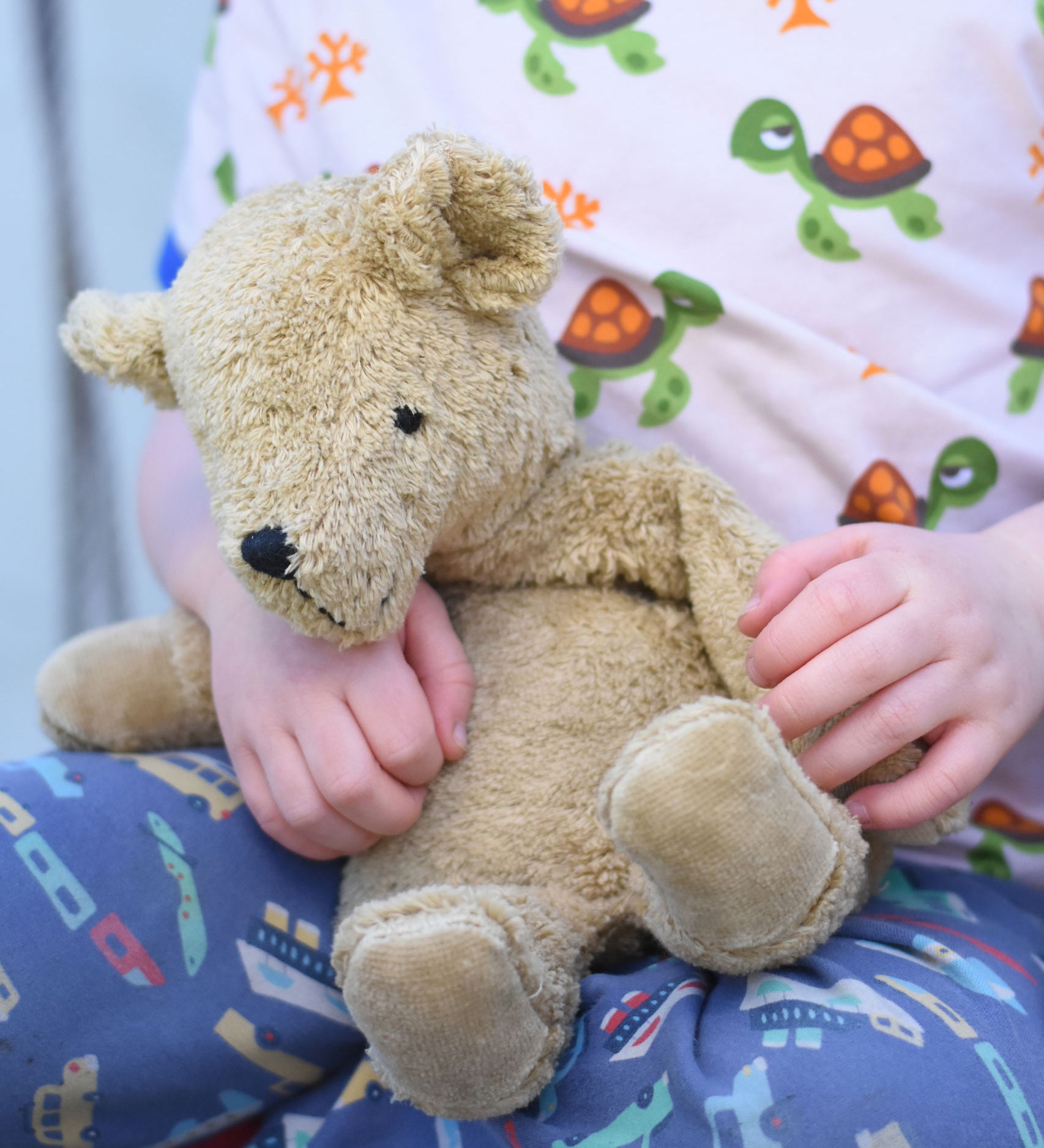 A close up of a small Senger beige cuddly teddy bear in a child's hands.