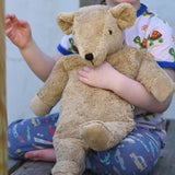 A close up of the large organic cotton Senger cuddly beige bear held in a child's arm.