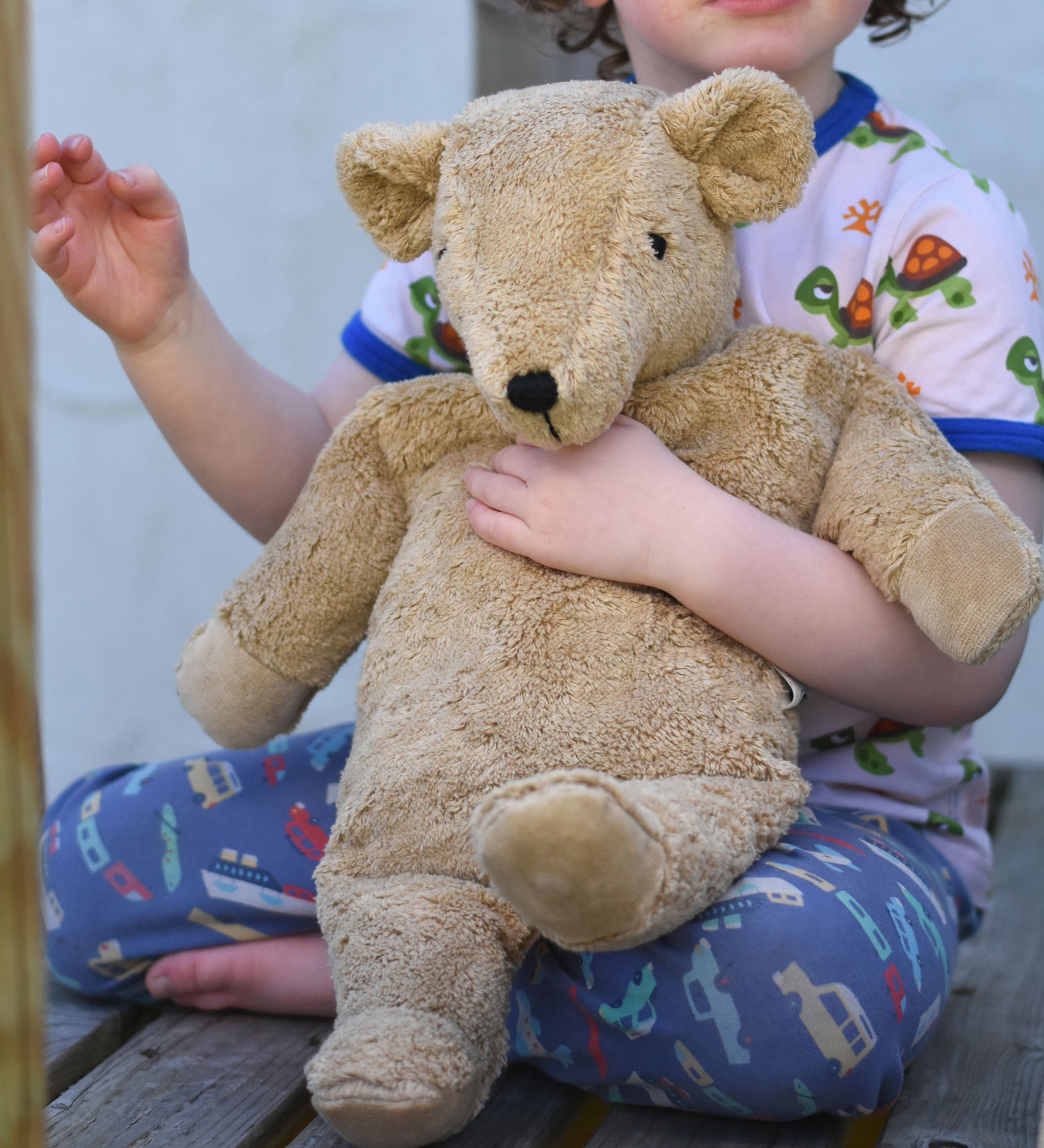 A close up of the large organic cotton Senger cuddly beige bear held in a child's arm.