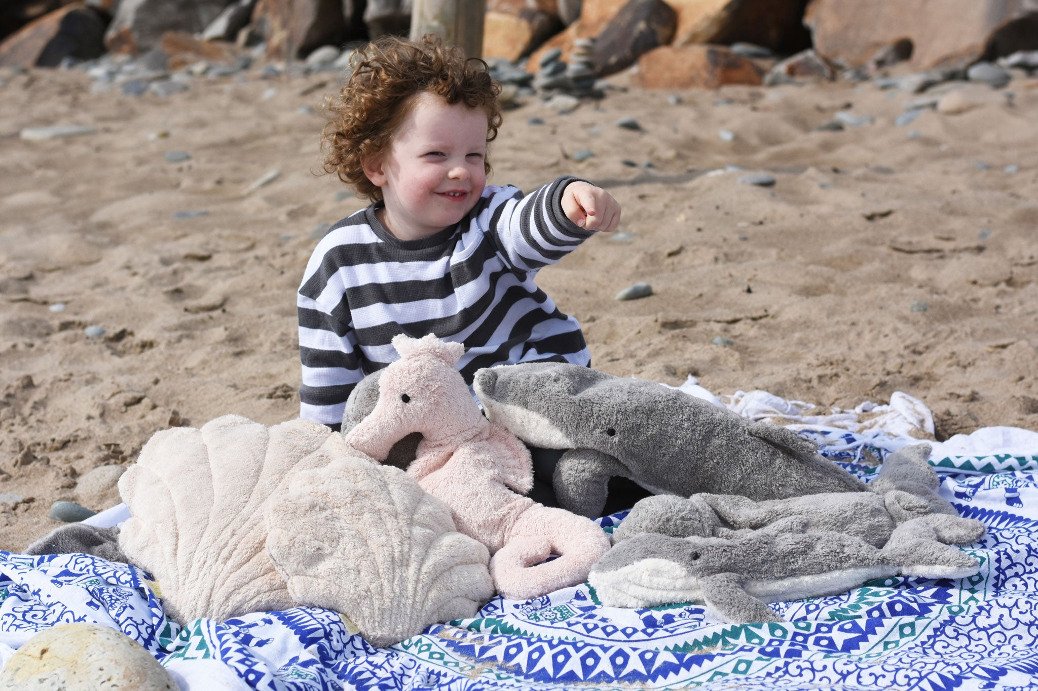 A child sitting on a blue and white patterned blanket with a  collection of sea life themed cuddly animals from Senger placed in front of them.