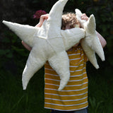A child holding up a small and large Senger starfish soft toys in front of his face. The Senger starfish are part of a wide range of organic soft toys available here at babipur. Made from organic materials and natural fillings.