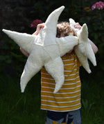 A child holding up a small and large Senger starfish soft toys in front of his face. The Senger starfish are part of a wide range of organic soft toys available here at babipur. Made from organic materials and natural fillings.