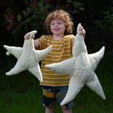 A child holding up a small and large Senger starfish soft toys in front of them. The Senger starfish are part of a wide range of organic soft toys available here at babipur.
