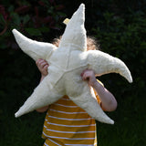 A child holding a large Senger starfish soft toy up in front of his face.  The 5 point starfish soft toy is made with organic and natural materials and fillings.