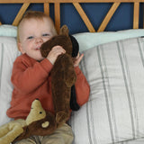 A child cuddling the Senger small floppy brown horse soft toy. There is a small floppy hedgehog soft toy resting on the child's knee.