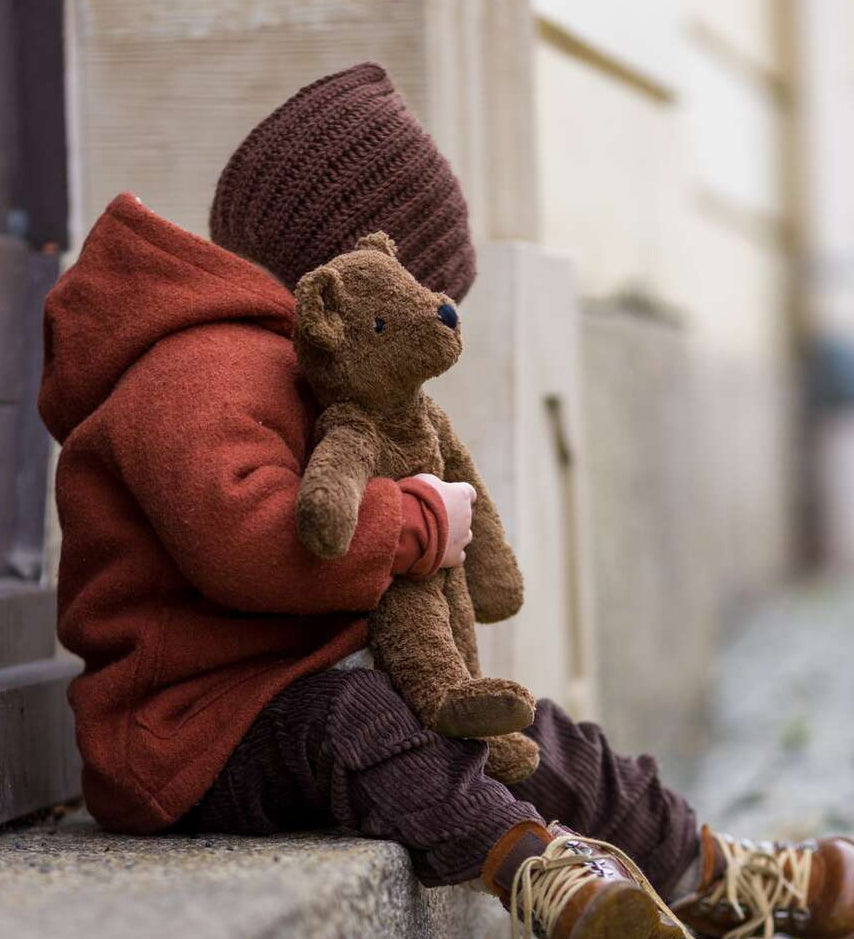 A toddler sat on a step, cuddling the Senger organic cotton loppy brown teddy bear