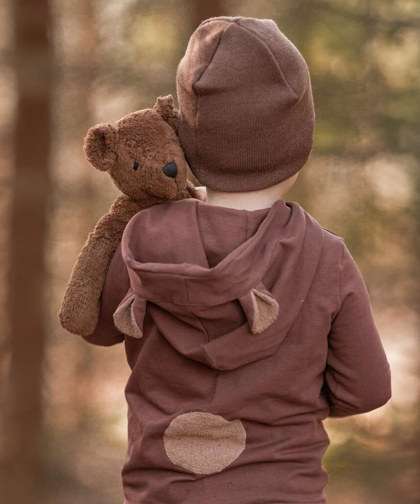 A toddler in the forest, holding the Senger organic cotton stuffed toy brown teddy bear