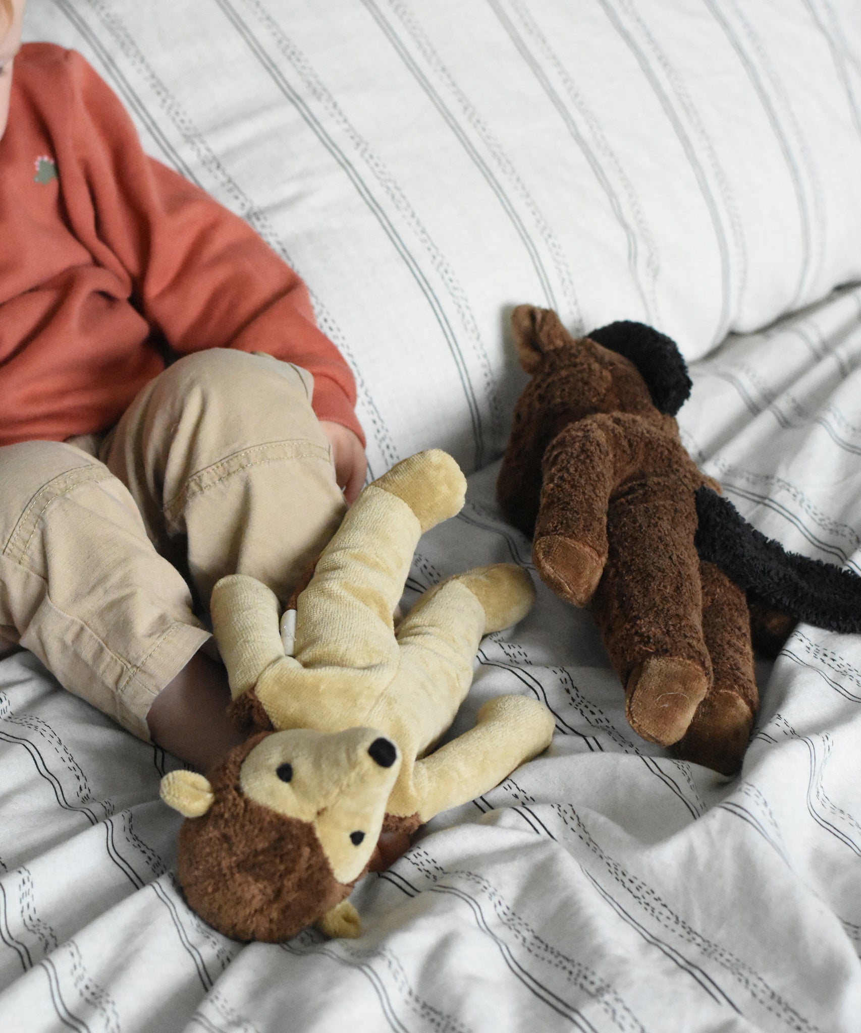 Two Senger soft toys placed on a cream and black striped duvet, a hedgehog and horse from Senger's floppy collection of soft toys made with organic cotton and natural fillings. A young child can be seen in the background.