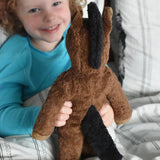 A child holding up the brown floppy horse soft toy from Senger showing the back of the animal. The horse has a brown body and a black mane and tail.