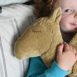 A close up of the face of the large Senger Cuddly Camel Organic Heatable Soft Toy. The camel is being cuddled by a child. The large camel soft toy is part of a wide selection of soft toys made from organic cotton and natural fillings available at Babipur.