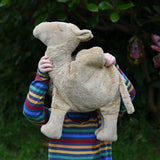 A child holding up the large Senger Cuddly Camel Organic Heatable Soft Toy. The child is wearing a striped rainbow coloured top.