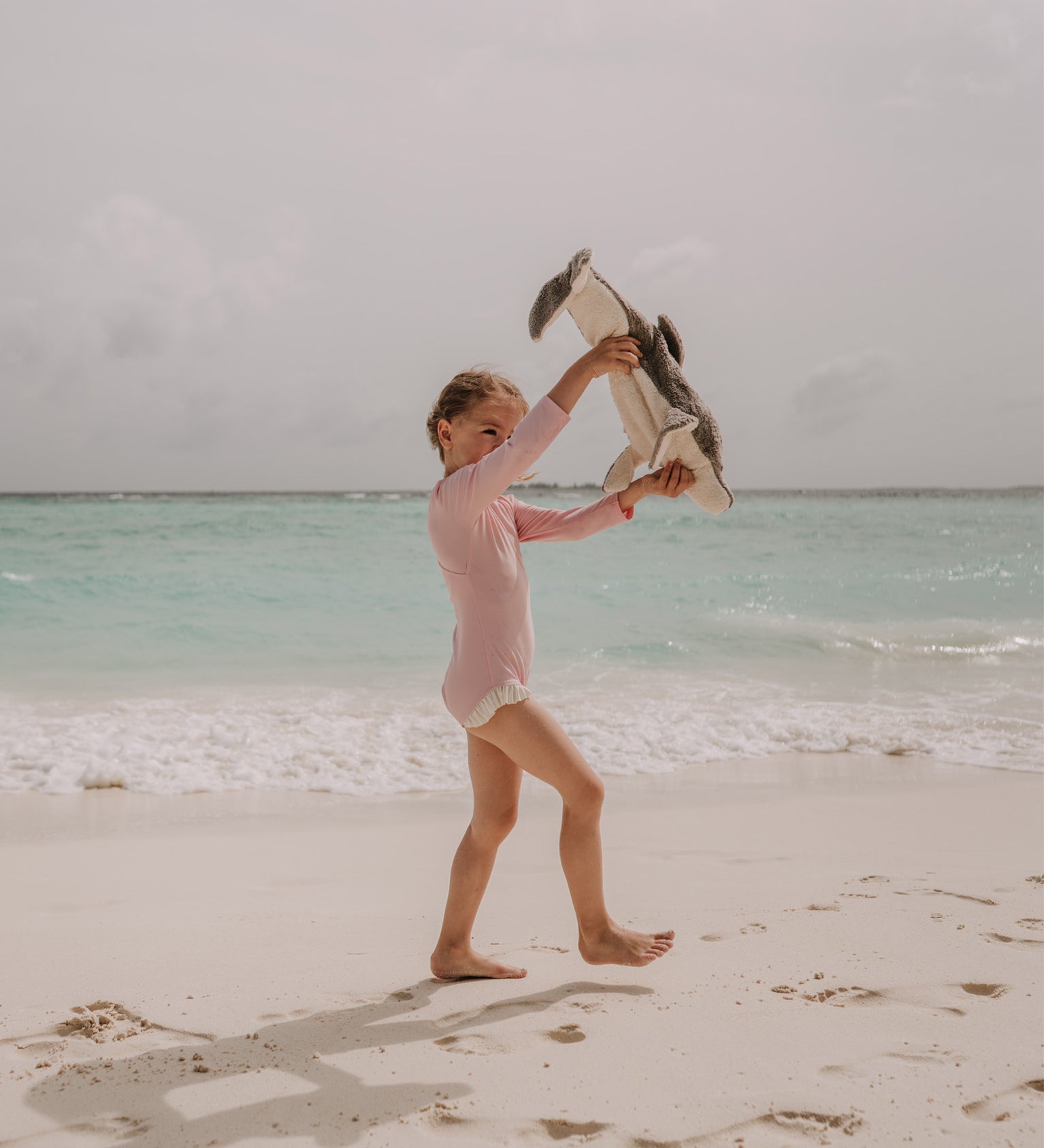 A little girl playing with the Senger large organic cotton stuffed dolphin toy on the beach