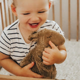 A toddler in a cot, cuddling the Senger small organic cotton stuffed camel toy