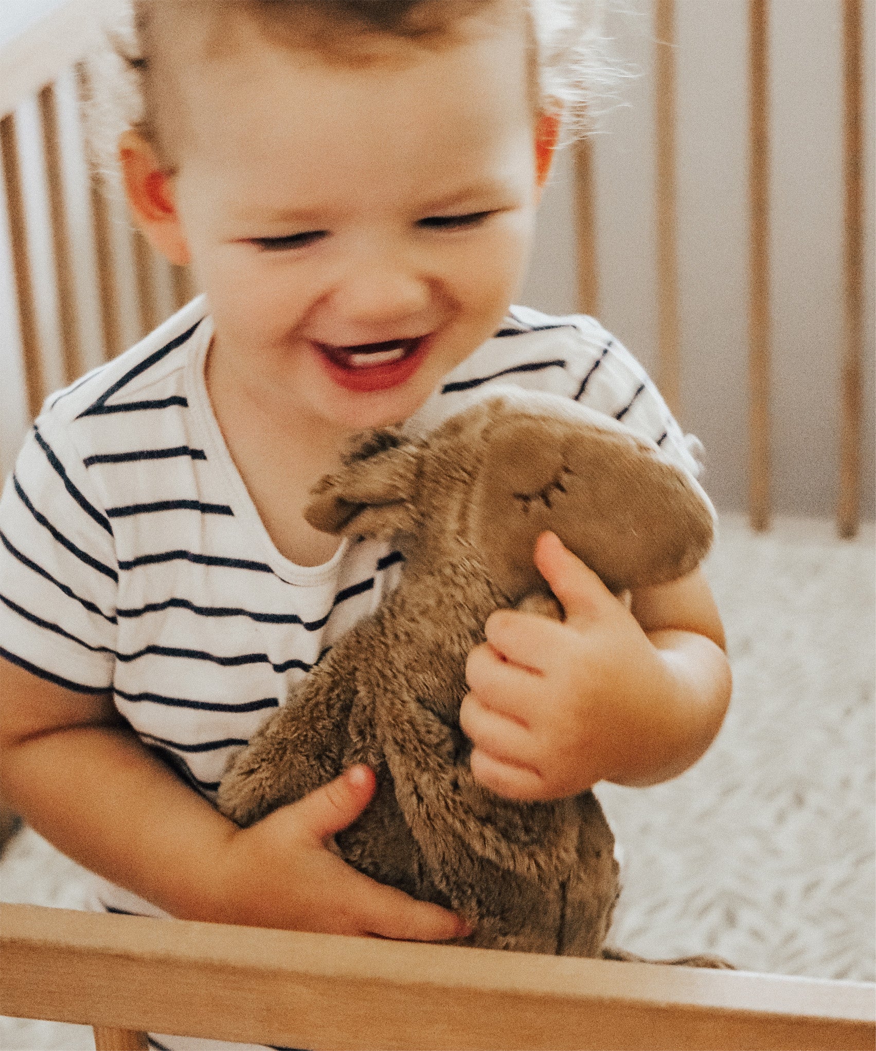 A toddler in a cot, cuddling the Senger small organic cotton stuffed camel toy