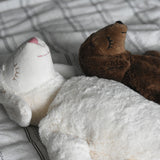 A Senger large white sheep and small brown sheep cuddly soft toys in laying positions on a cream and black striped duvet. These sheep are part of a wide range of soft toys made from organic and natural materials stocked at Babipur.