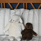 A Senger large white sheep and small brown sheep soft toy in seated position next to each other, leaning against pillows and a wooden headboard. These sheep are part of a wide range of soft toys made from organic and natural materials stocked at Babipur.