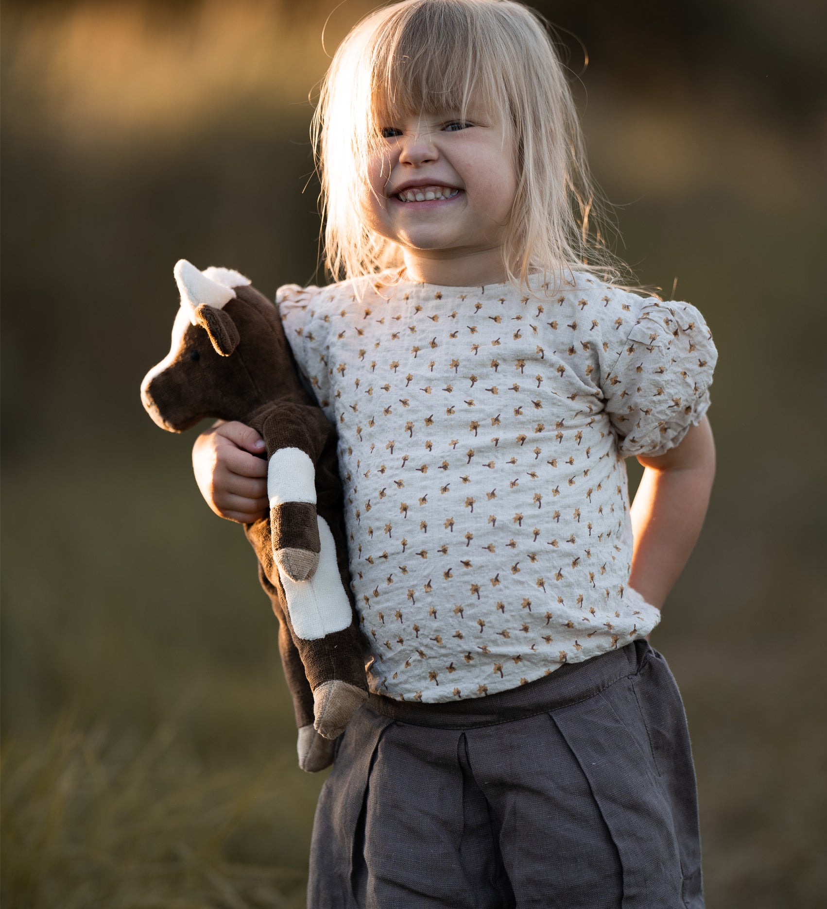 A little girls in a field, holding the Senger organic cotton floppy cow stuffed animal toy.