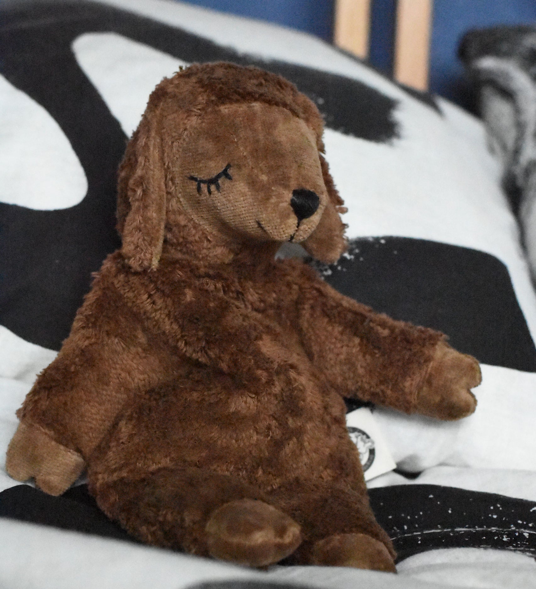 A Senger small brown cuddly sheep organic soft toy placed on a black and white monochrome patterned duvet. The small brown sheep is part of Senger's cuddly range of soft toys available at Babipur.
