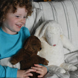 A child holding the Senger small brown cuddly sheep soft toy on their  lap in bed. A large white cuddly sheep can be seen next to the child. These sheep are part of a wide range of soft toys made from organic and natural materials stocked at Babipur.