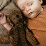 A baby laying next to a Senger Small Cuddly Sheep - Brown.