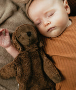 A baby laying next to a Senger Small Cuddly Sheep - Brown.