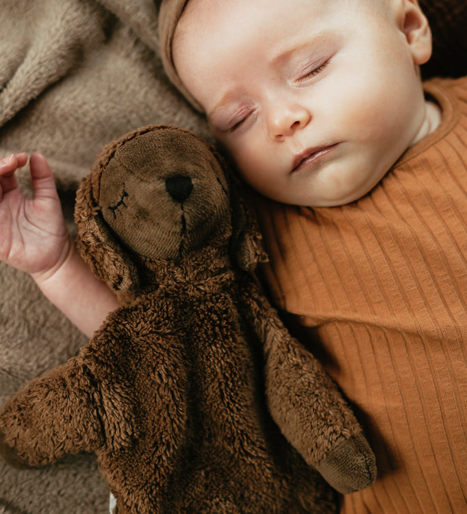 A baby laying next to a Senger Small Cuddly Sheep - Brown.