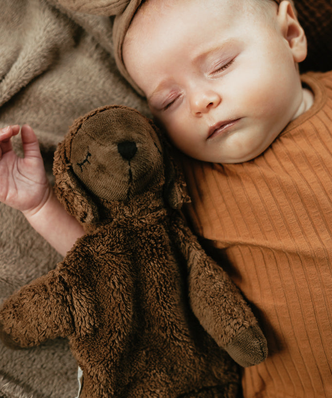 A baby laying next to a Senger Small Cuddly Sheep - Brown.
