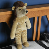 A Senger small floppy hedgehog soft toy placed in a standing position against a wooden headboard on a pillow. This hedgehog is part of a wider selection of soft toys made with organic cotton and natural fillings that are available at Babipur.
