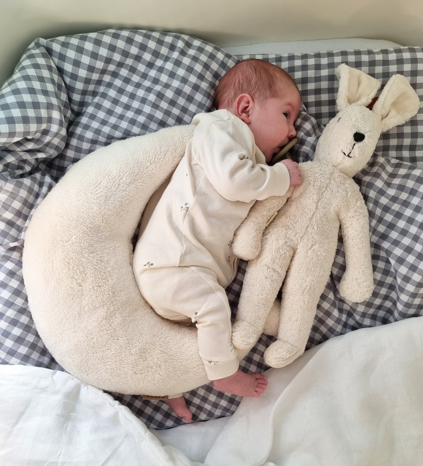 A small baby laying next to a white Senger Small Floppy Rabbit.