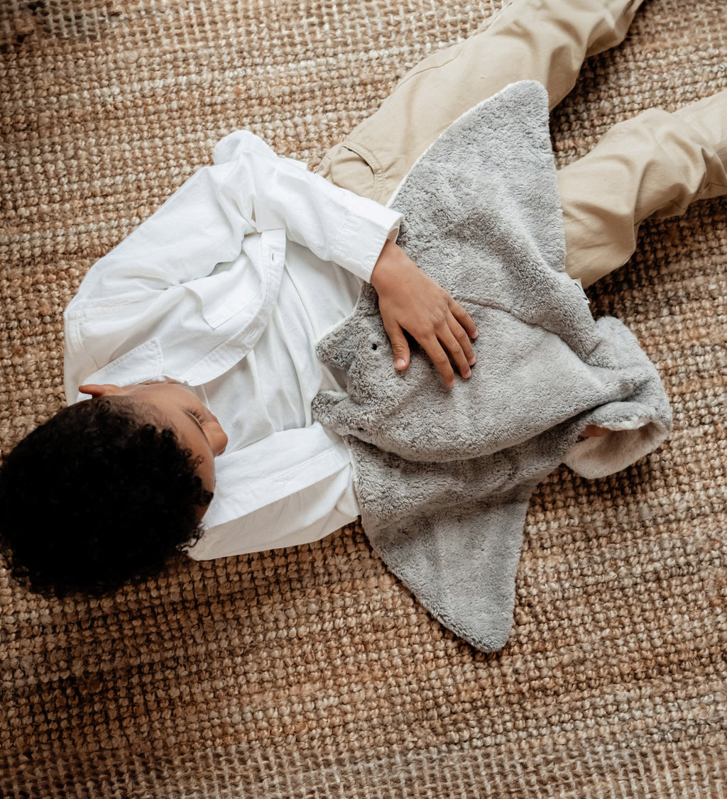 A view looking down on a little boy, cuddling the Senger large organic cotton grey manta ray heatable cuddly toy